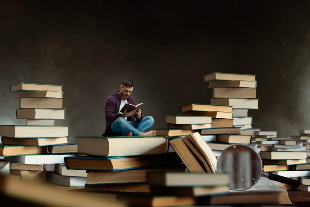 בחור צעיר יושב על ערימה ענקית של ספרים וקורא ספר