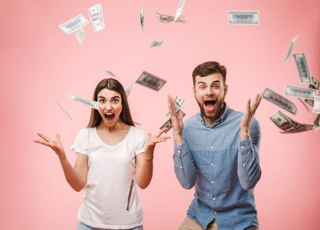 גבר ואישה צעירים זורקים כסף באוויר על רקע ורוד