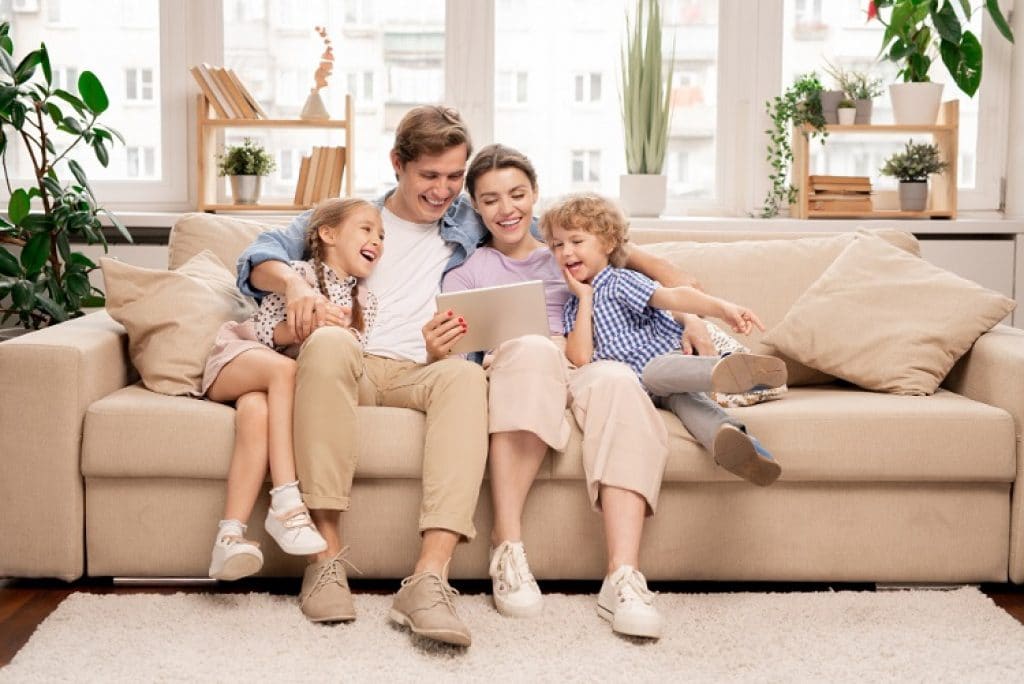 משפחה של גבר אישה ושני ילדים יושבים בסלון ומסתכלים על טאבלט